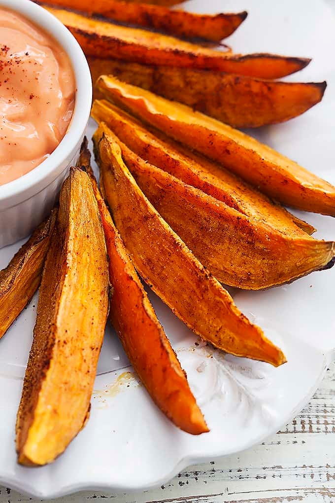 close up of spicy baked sweet potato wedges on a plate with a dipping bowl of fry sauce on the side.