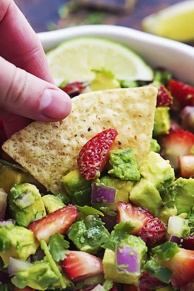 close up of a hand dipping a chip in a bowl of strawberry avocado salsa.