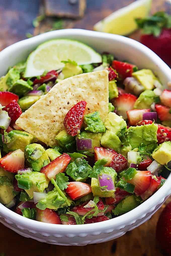close up of strawberry avocado salsa in a bowl with a chip dipped inside.