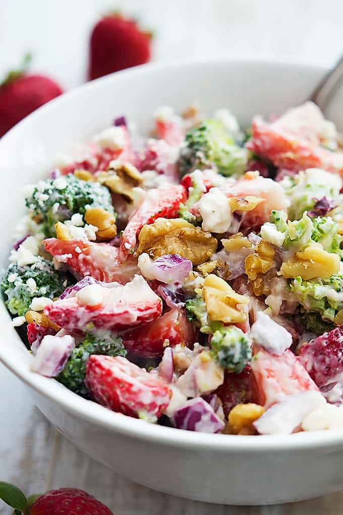 strawberry broccoli salad in a bowl with whole strawberries in the background.