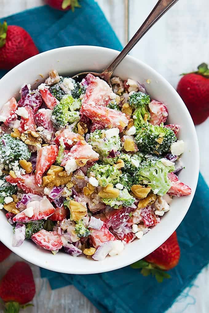 top view of strawberry broccoli salad and a spoon in a bowl surrounded by whole strawberries.