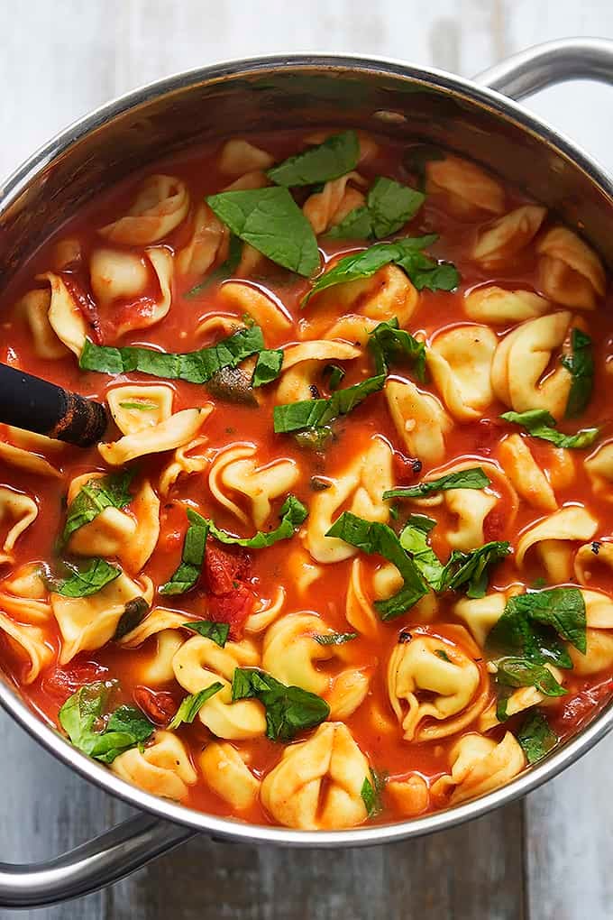 top view of tomato spinach tortellini soup and a serving spoon in a cooking pot.