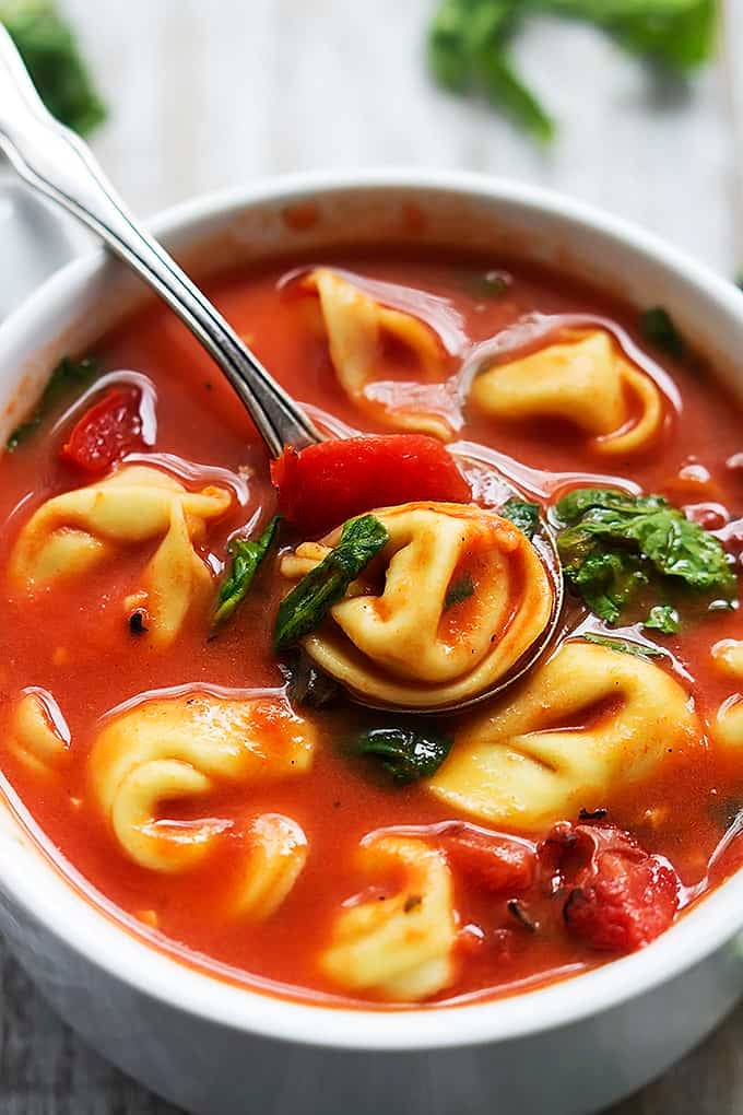 tomato spinach tortellini soup in a bowl with a spoon sitting on top with a spoonful of soup on it.