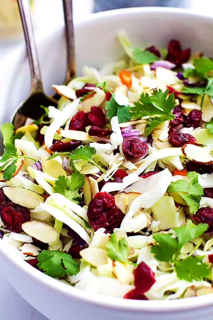 close up of Asian cranberry almond salad + sesame dressing with two serving spoons in a bowl.