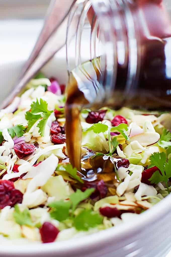 sesame dressing being poured on top of Asian cranberry almond salad in a bowl.