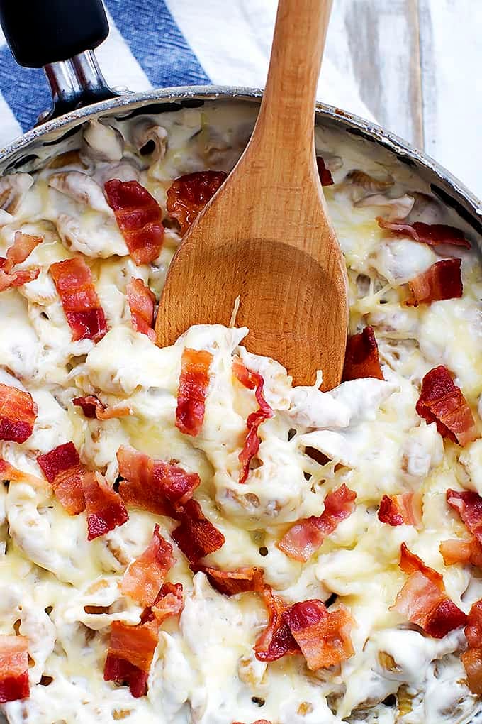 close up top view of cheesy bacon alfredo shells with a wooden serving spoon in a skillet.