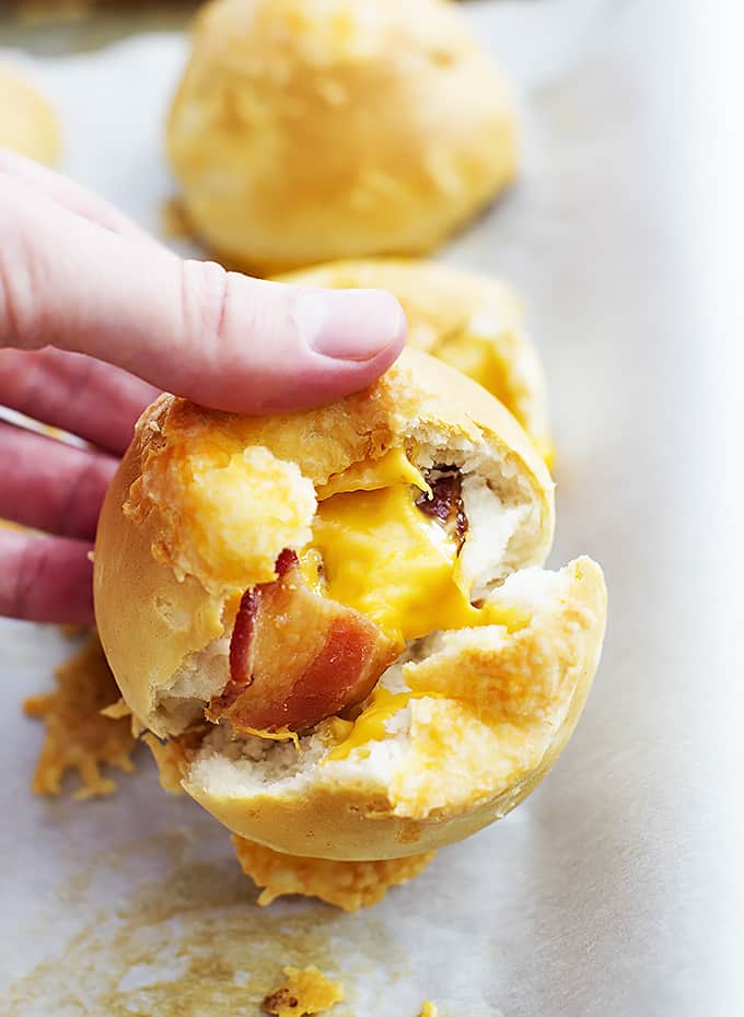 a hand holding a cheddar bacon bomb opened up with more bombs on the side.