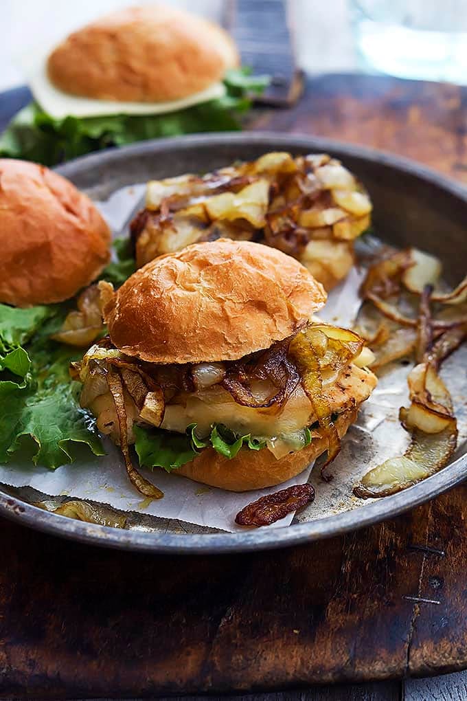 French onion chicken sliders and onions on a round serving tray with another slider in the background.