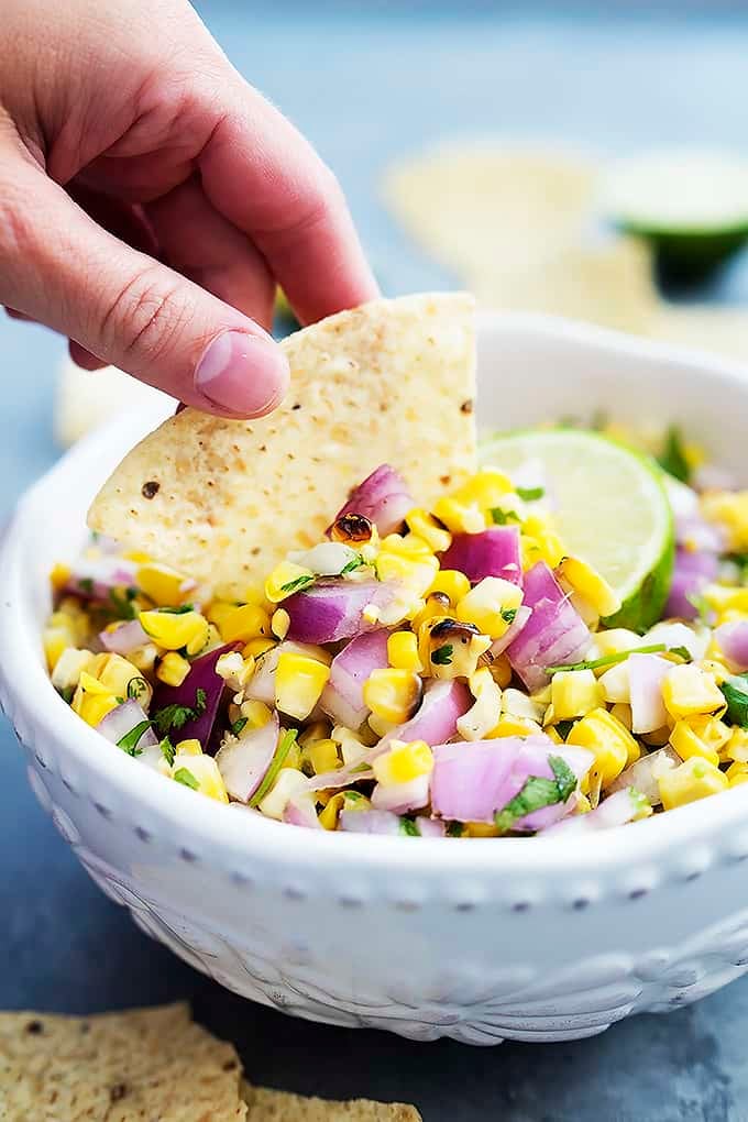 a hand dipping a chip in a bowl of grilled corn salsa.