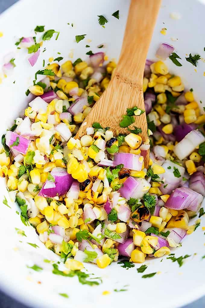 top view of grilled corn salsa with a wooden serving spoon in a bowl.