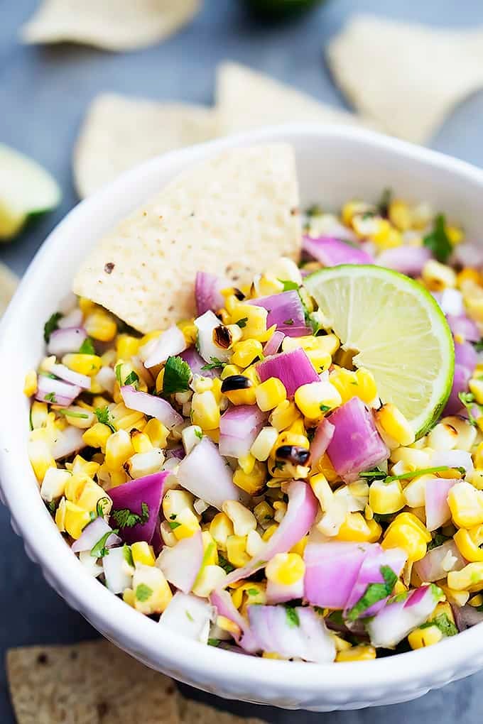 a bowl of grilled corn salsa with a chip dipped in it.