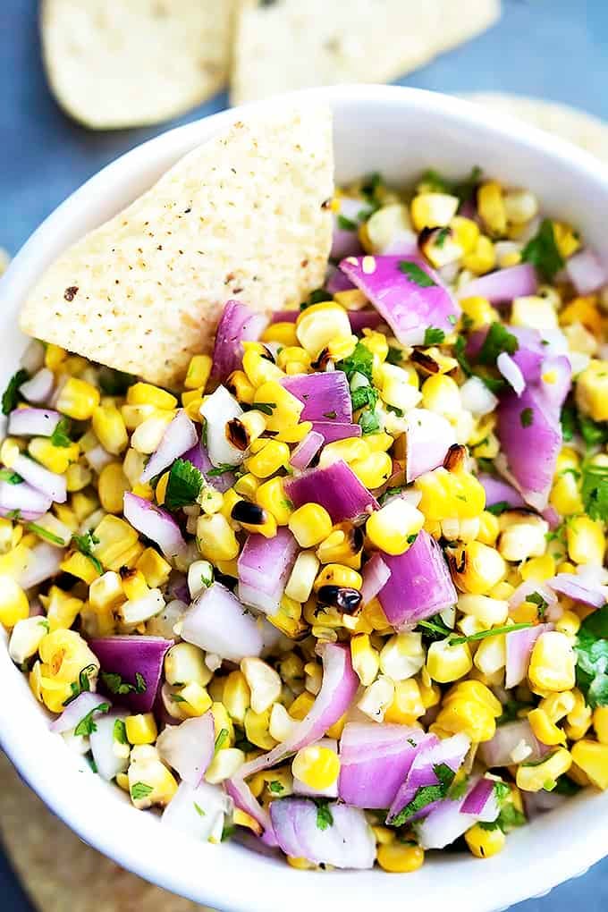 top view of grilled corn salsa in a bowl with a chip dipped in it.