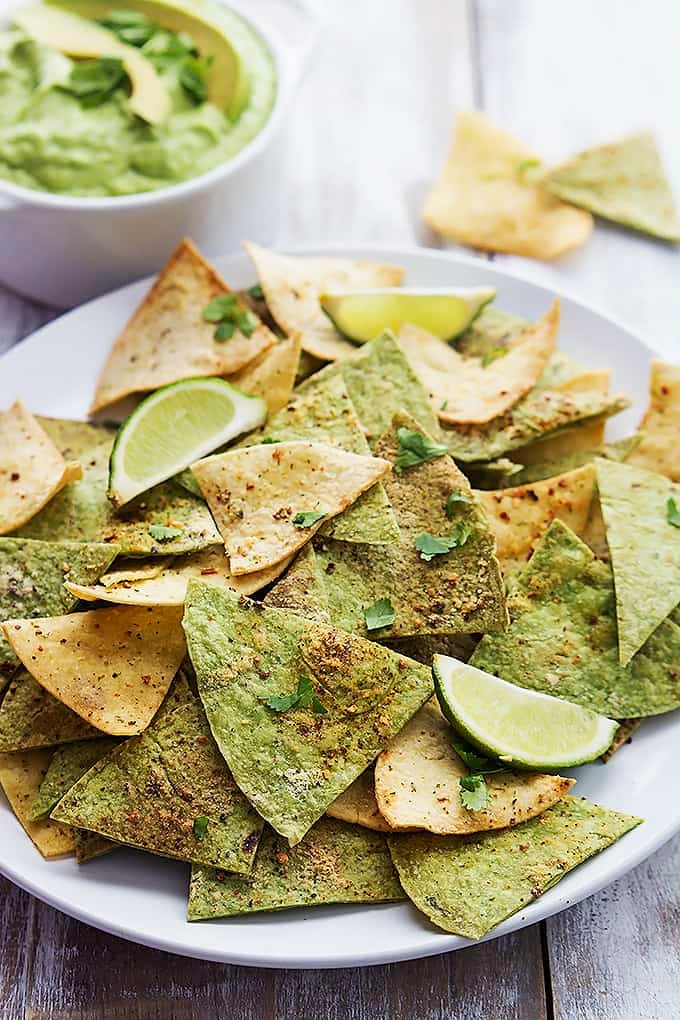 baked guacamole tortilla chips with lime slices on a plate with a bowl of guacamole on the side.