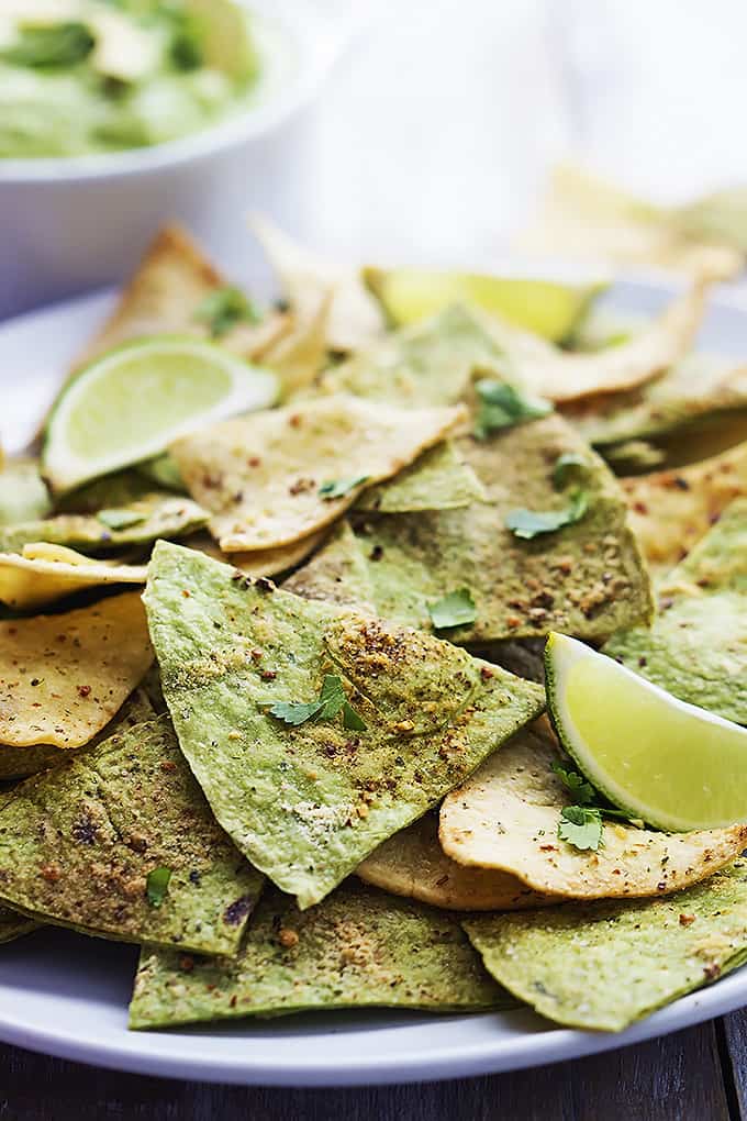 close up of baked guacamole tortilla chips and lime slices on a plate.