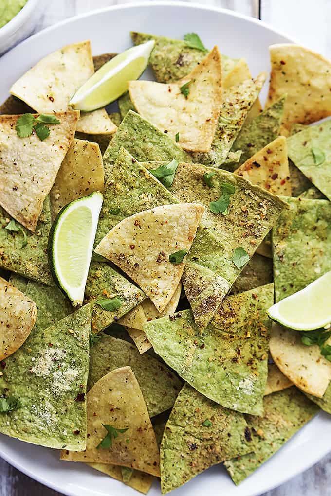 close up top view of baked guacamole tortilla chips with lime slices on a plate.