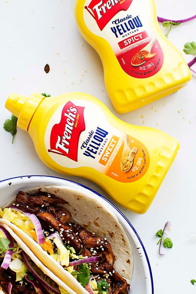 spicy mustard bottles with a plate of slow cooker Korean bbq pork tacos on the side.
