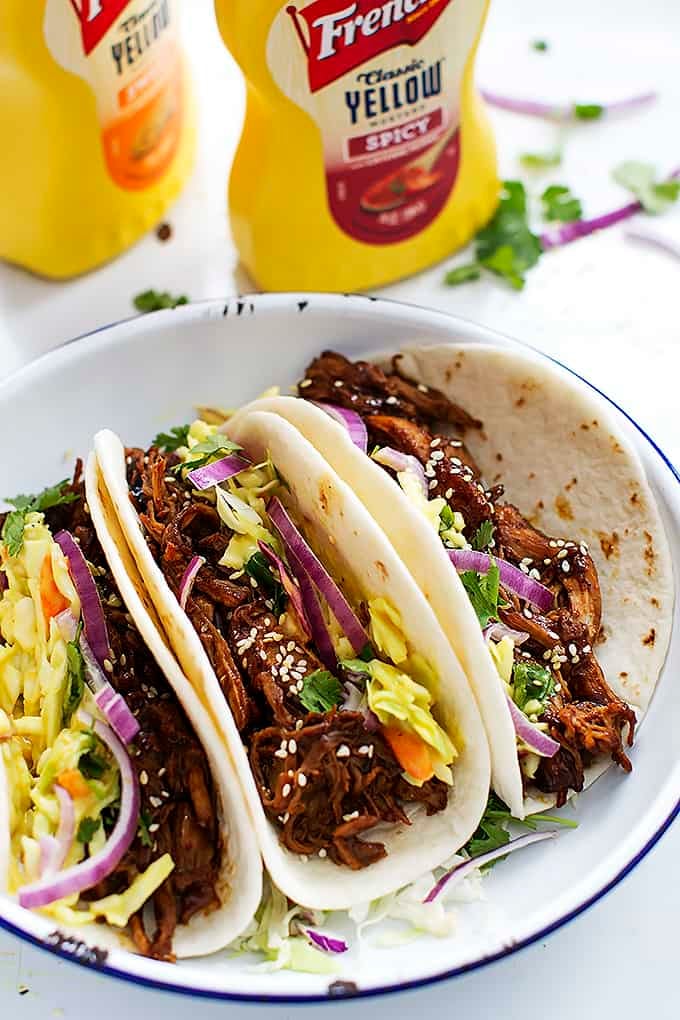 slow cooker Korean bbq pork tacos on a plate with spicy mustard bottles in the background.
