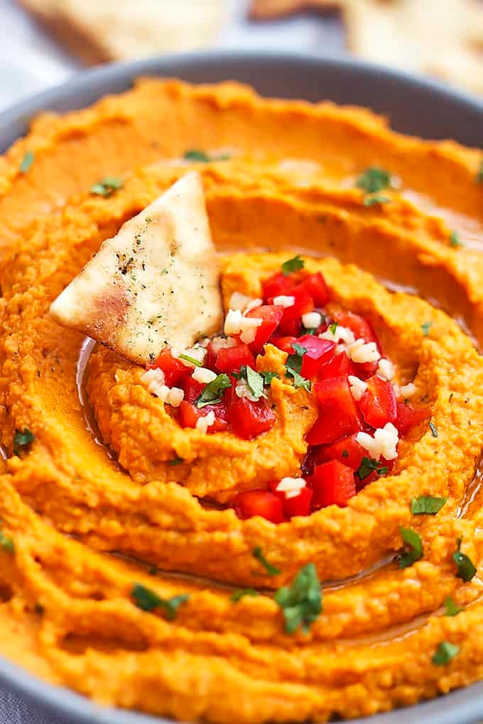 close up roasted red pepper hummus in a bowl with a chip dipped inside.