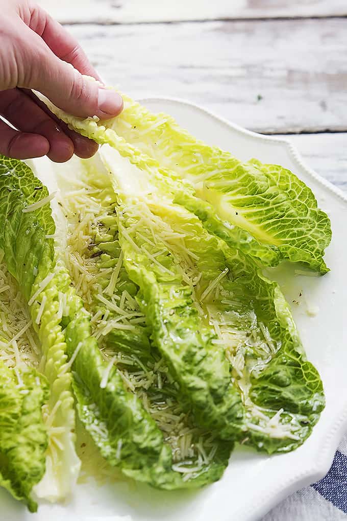 a hand picking up a piece of romaine finger salad from a plate.