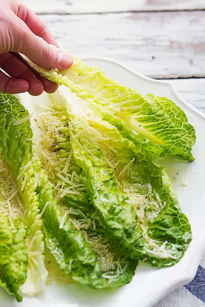 a hand picking up a piece of romaine finger salad from a plate.