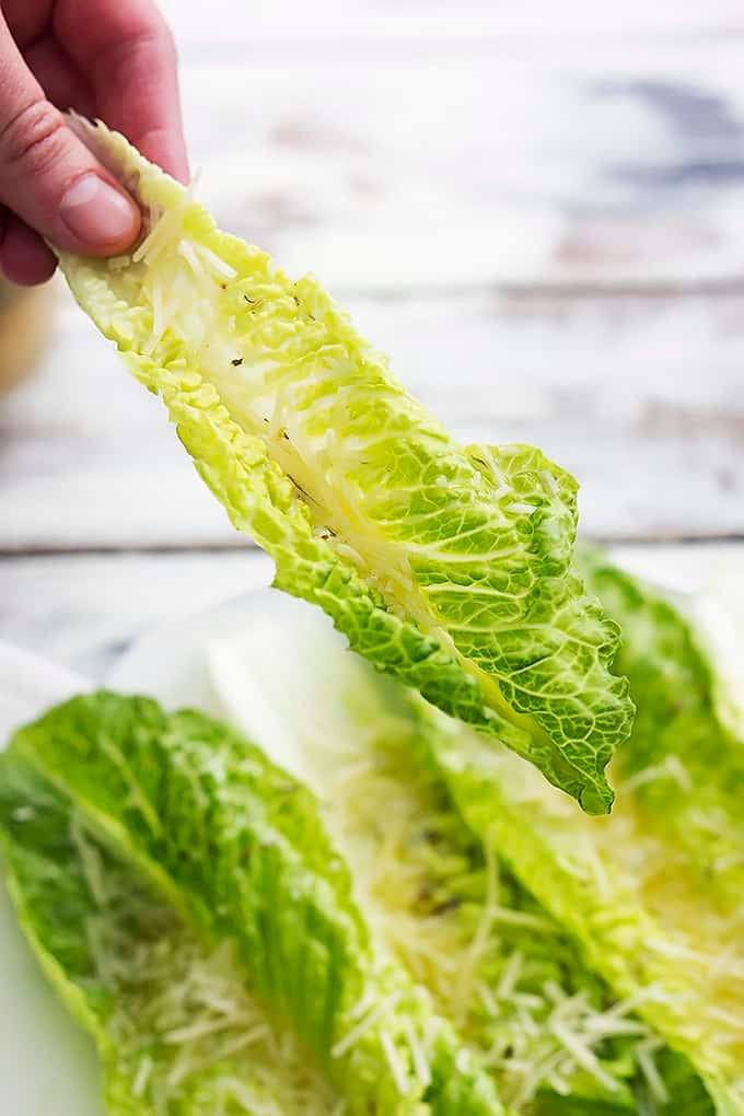 a hand holding a piece of romaine finger salad above a plate of salad.