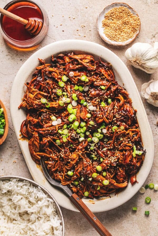 Overhead of slow cooker honey soy shredded chicken and a fork on a white oval platter.