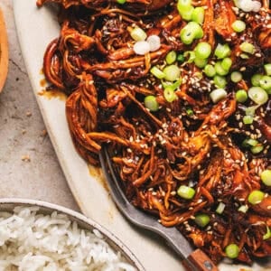 Overhead close up of slow cooker honey soy shredded chicken and a fork on a white oval platter.