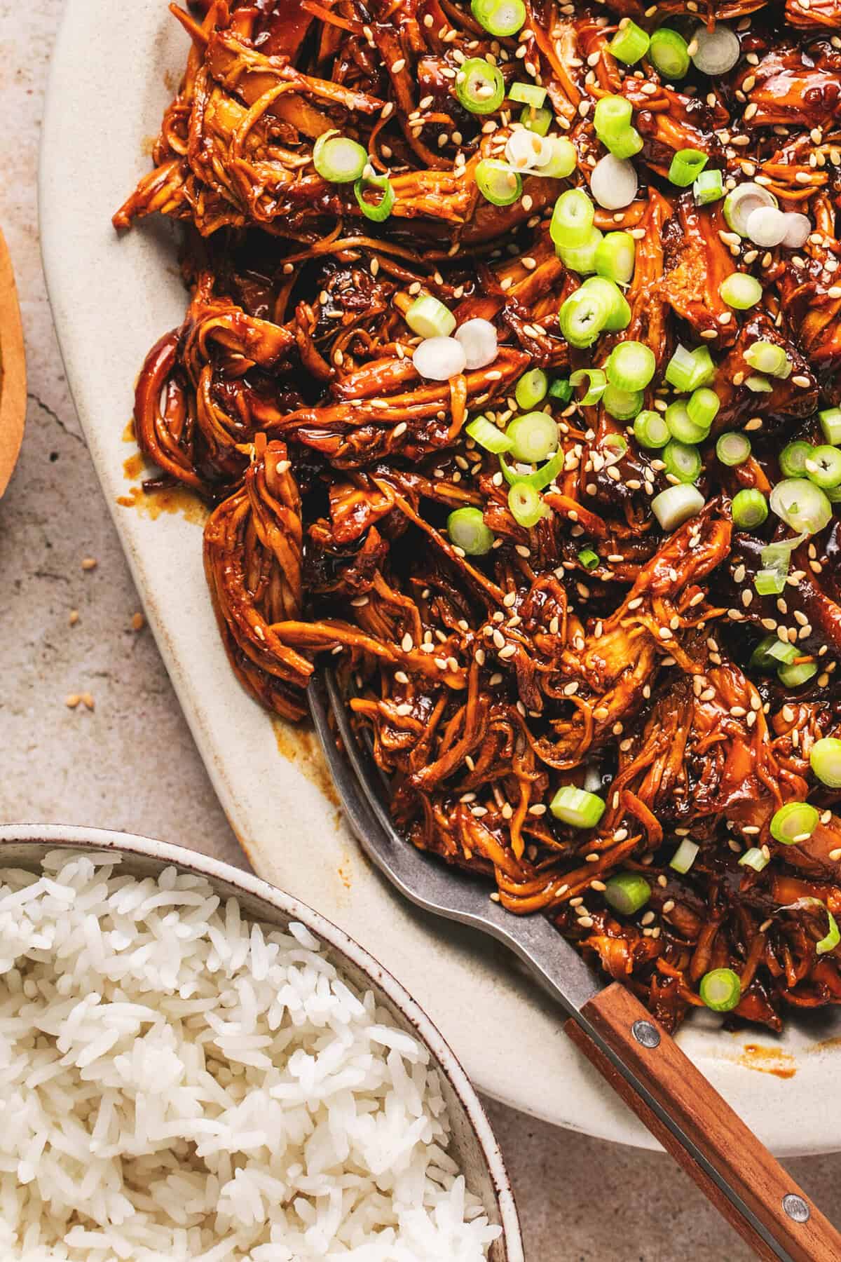 Overhead close up of slow cooker honey soy shredded chicken and a fork on a white oval platter.