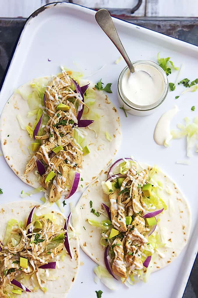 top view of slow cooker ranch chicken tacos and a jar of creamy ranch dressing with a spoon in it all on a baking sheet.
