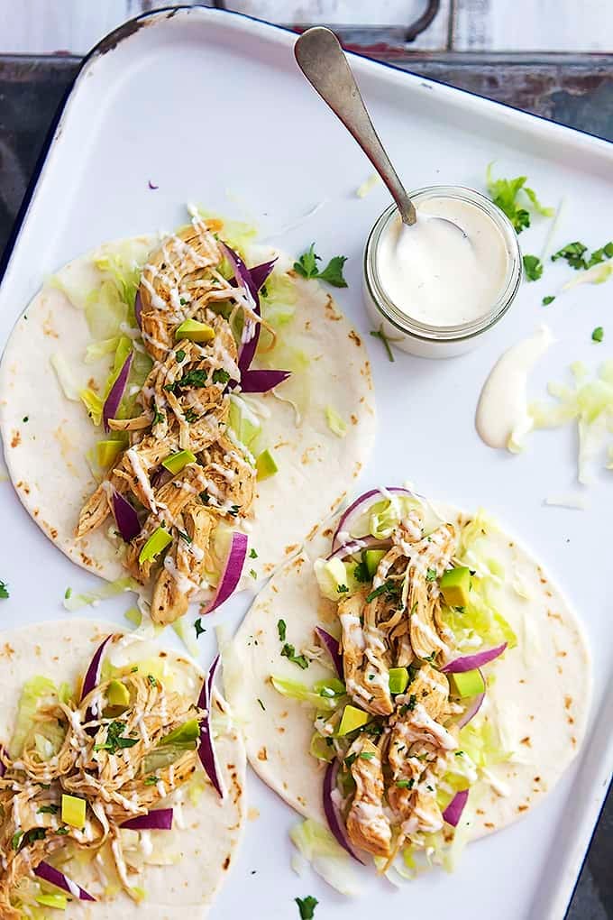 top view of slow cooker ranch chicken tacos and a jar of creamy ranch dressing with a spoon in it all on a baking sheet.