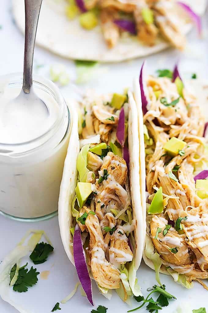 slow cooker ranch chicken tacos with a jar of creamy ranch with a spoon on the side.