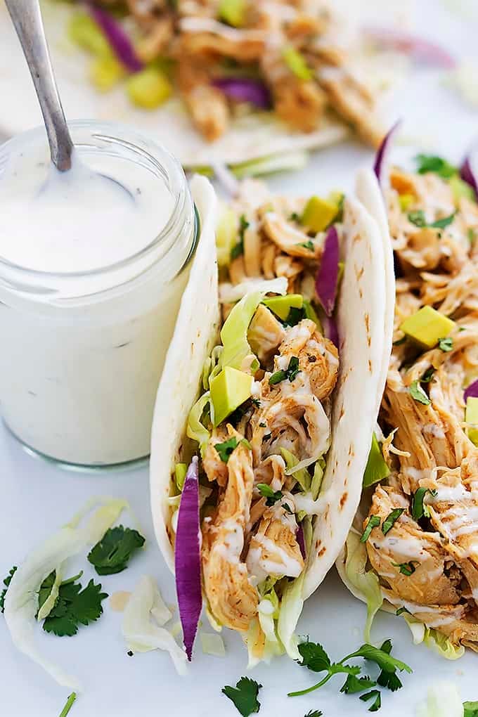 slow cooker ranch chicken tacos with a jar of creamy ranch dressing with a spoon in it.