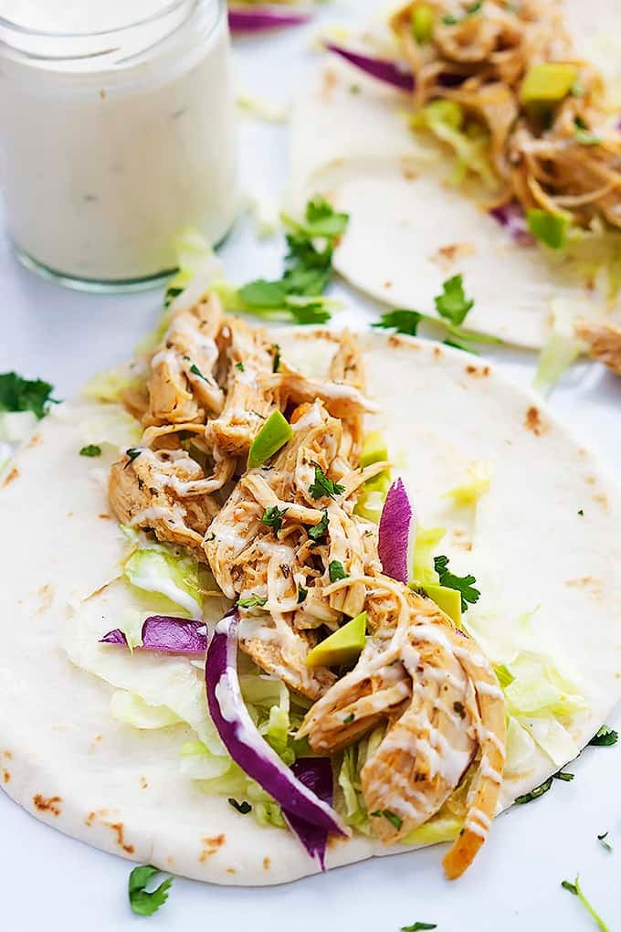 a slow cooker ranch chicken taco with a jar of creamy ranch dressing and another taco in the background.