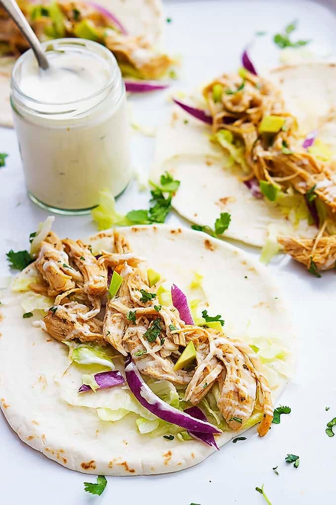 slow cooker ranch chicken tacos with a jar of creamy ranch dressing with a spoon in it.