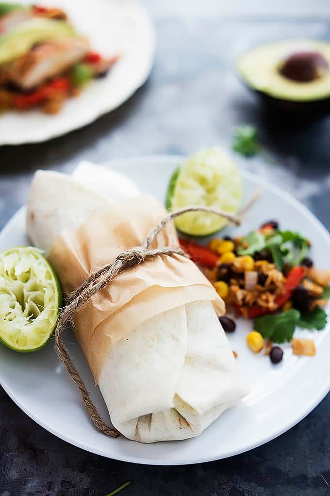 a Southwest chicken burrito wrapped in paper with squeezed lime halves all on a plate.