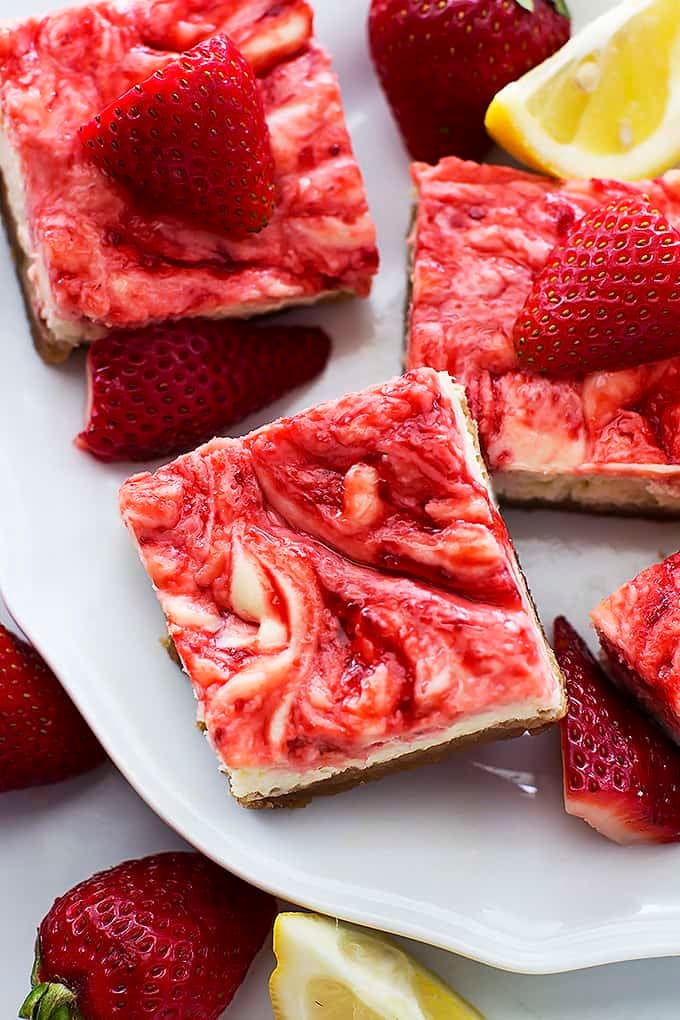 close up top view of strawberry lemon cheesecake bars on a plate with strawberries and lemon slices around the bars and plate.