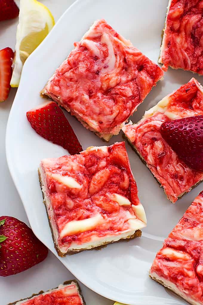 top view of strawberry lemon cheesecake bars on a plate with strawberries and lemon slices on the side.