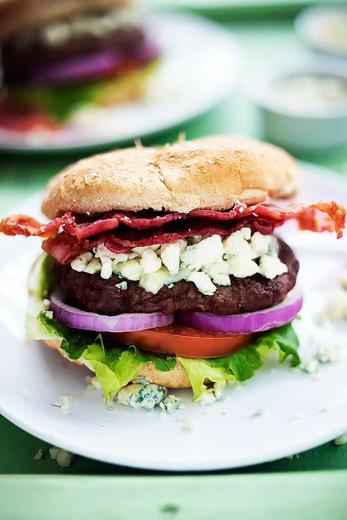a bacon blue cheese burger on a plate with another burger on a plate in the background.
