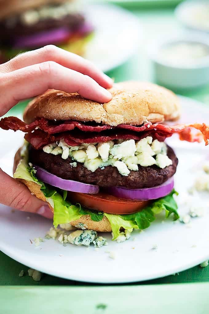 a hand grabbing a bacon blue cheese burger from a plate.