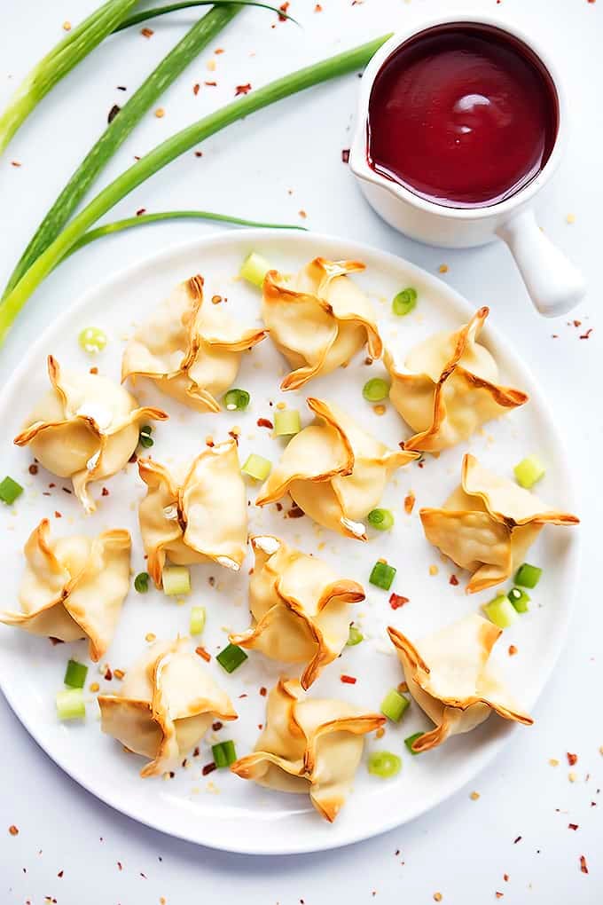 top view of baked cream cheese wontons on a plate with sauce on the side.