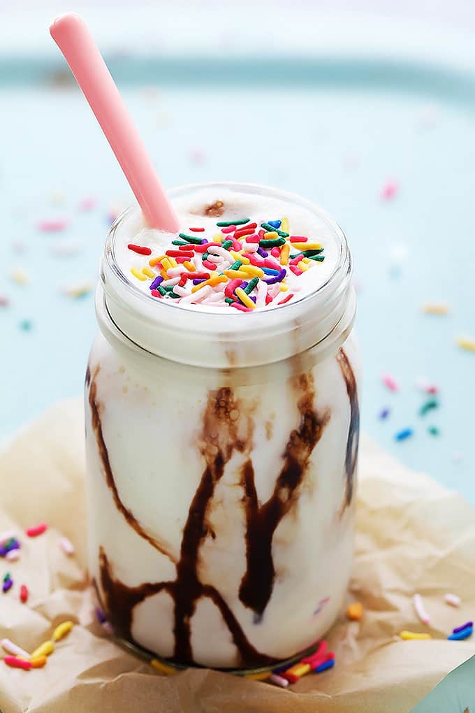 cake batter smoothie with a pink spoon in a mason jar with sprinkles around it.