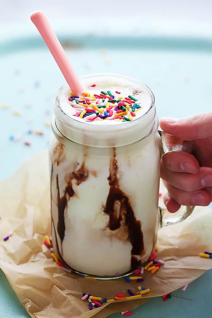 a hand holding the handle of a mason jar full of cake batter smoothie with a pink spoon in it.