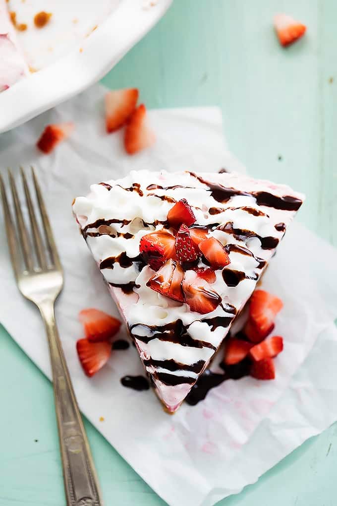 top view of a slice of frozen strawberry cheesecake topped with cream, chocolate syrup and chopped strawberries with a fork on the side.