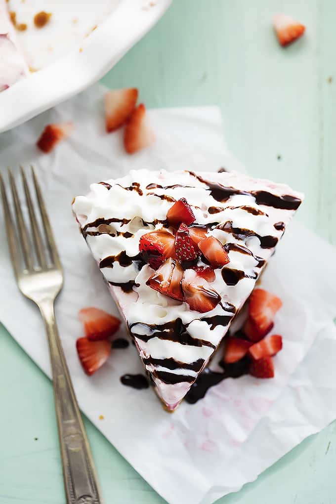 top view of a slice of frozen strawberry cheesecake topped with cream, chocolate syrup and chopped strawberries with a fork on the side.