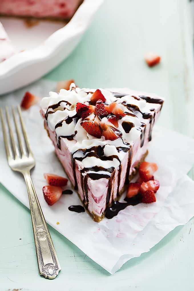 frozen strawberry cheesecake topped with cream, chocolate syrup and chopped strawberries with a fork on the side.