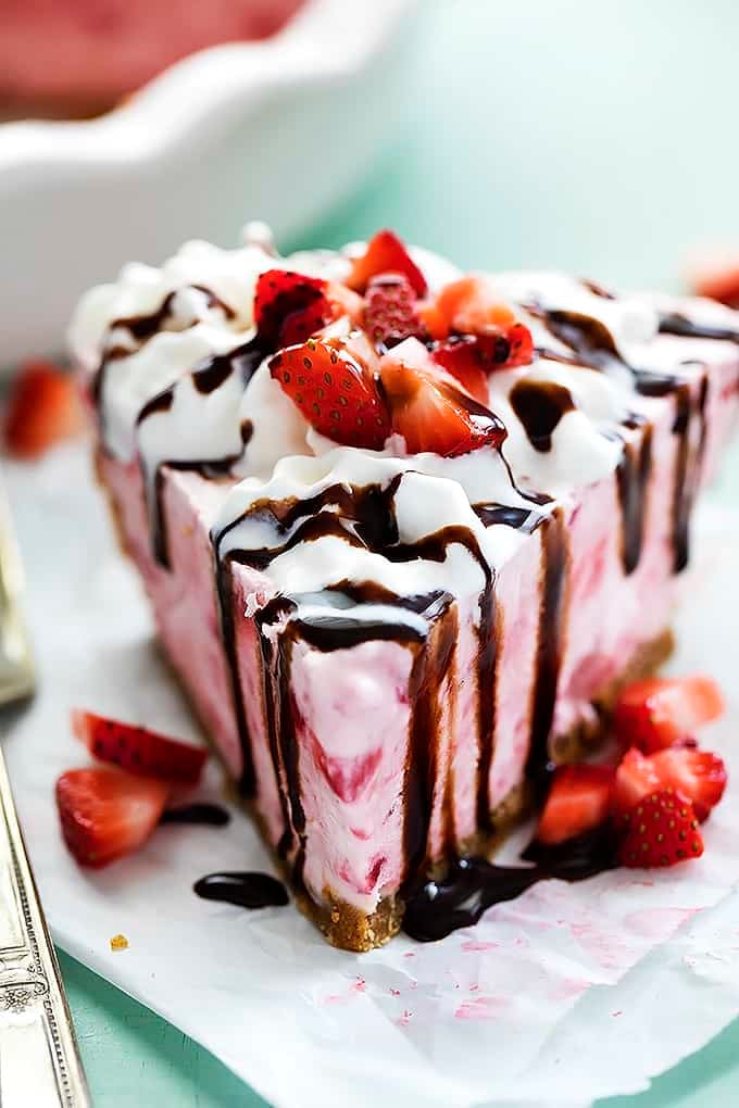a slice of frozen strawberry cheesecake topped with cream, chocolate sauce and chopped strawberries.
