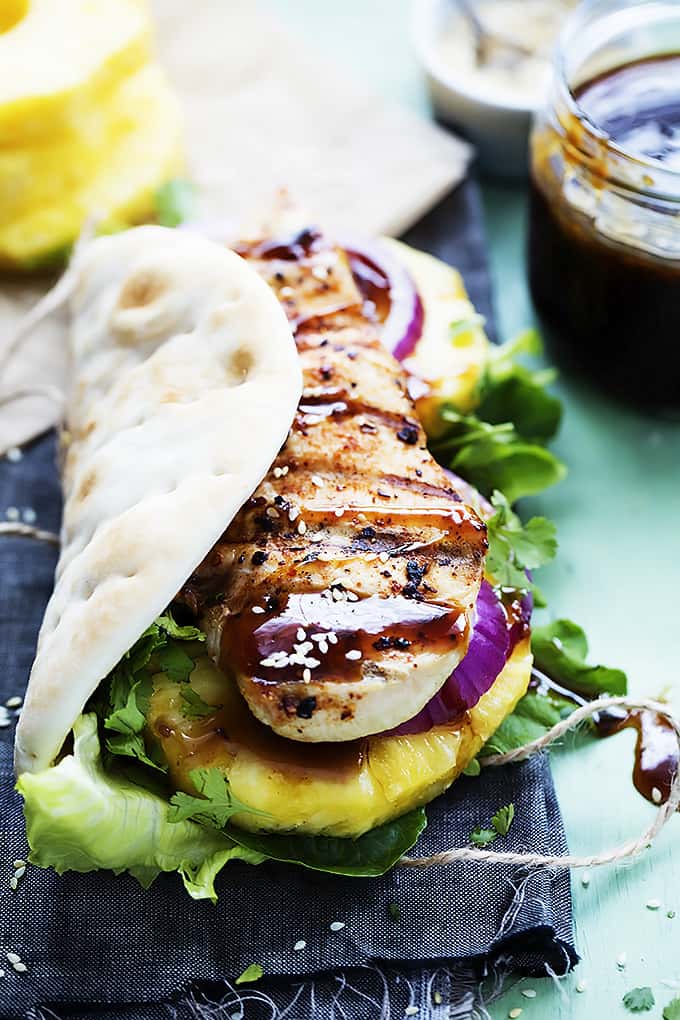 close up of a grilled pineapple teriyaki chicken wrap with pineapple slices and a jar of sauce in the background.