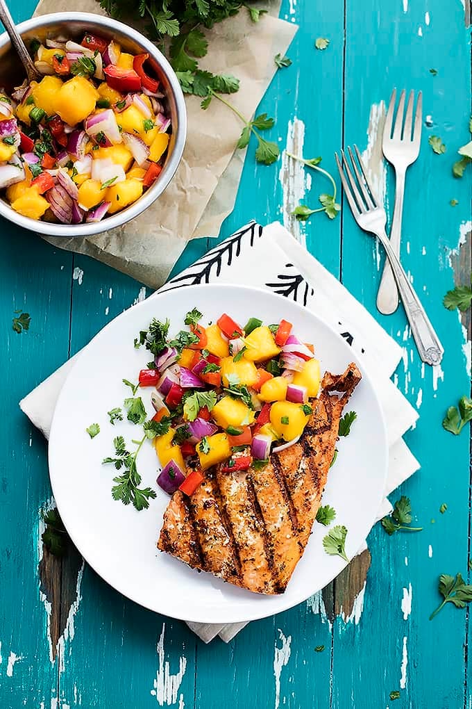 top view of grilled salmon with mango salsa on a plate with forks and a bowl of salsa on the side.