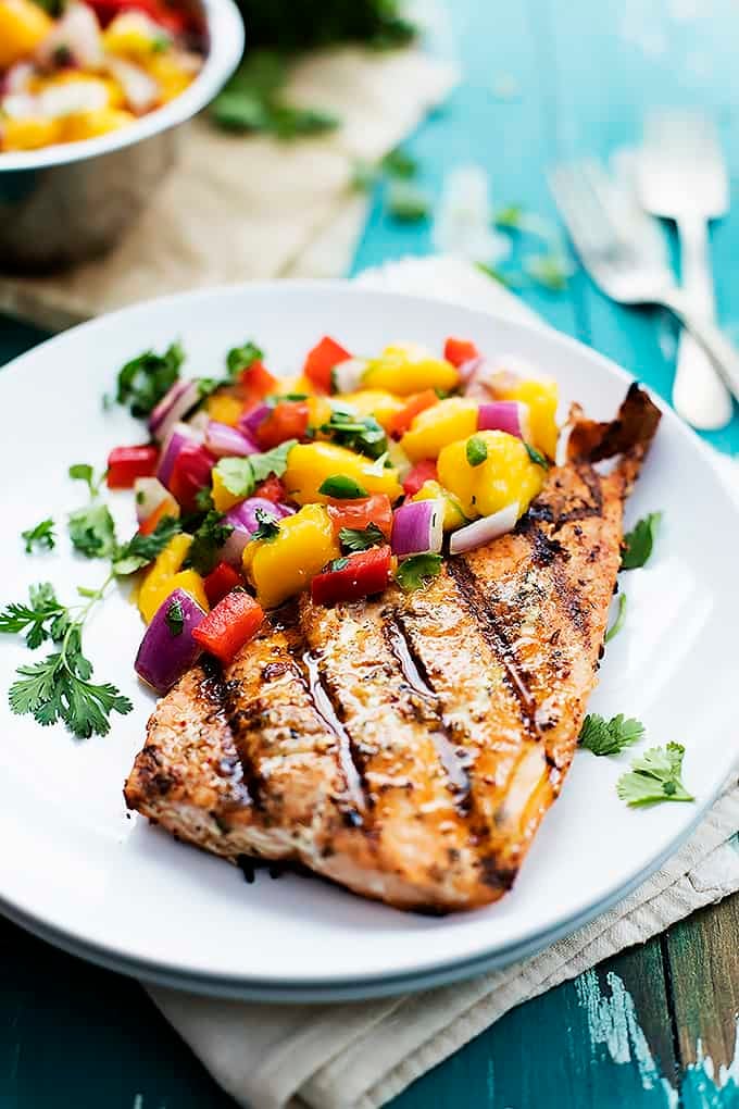 grilled salmon with mango salsa on a plate with forks and a bowl of salsa in the background.