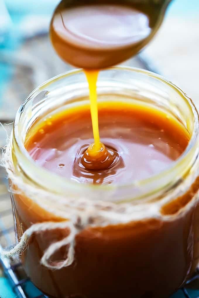 close up of a spoon lifting up a spoonful of caramel sauce from a jar of caramel sauce.